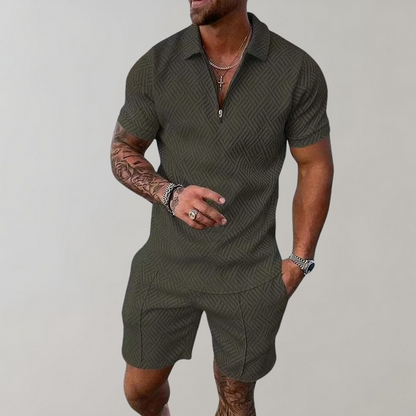 Mann in olivgrünem, gemustertem Kurzarm-Overall mit Reißverschluss, tätowierten Armen und Schmuck. Modetrend, Herrenmode, Sommeroutfit.