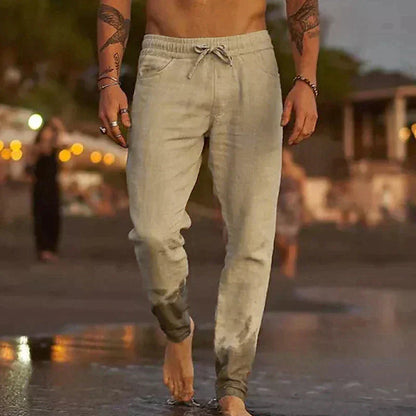 Mann in nasser, hellgrauer Jogginghose am Strand bei Sonnenuntergang, barfuß im Wasser. Freizeitmode, Sommerabend, Strandspaziergang.