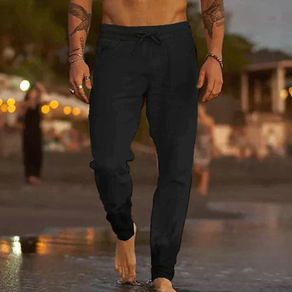 Mann in schwarzen Jogginghosen am Strand bei Sonnenuntergang, barfuß gehend. Freizeitmode, Strandspaziergang, Abendstimmung.
