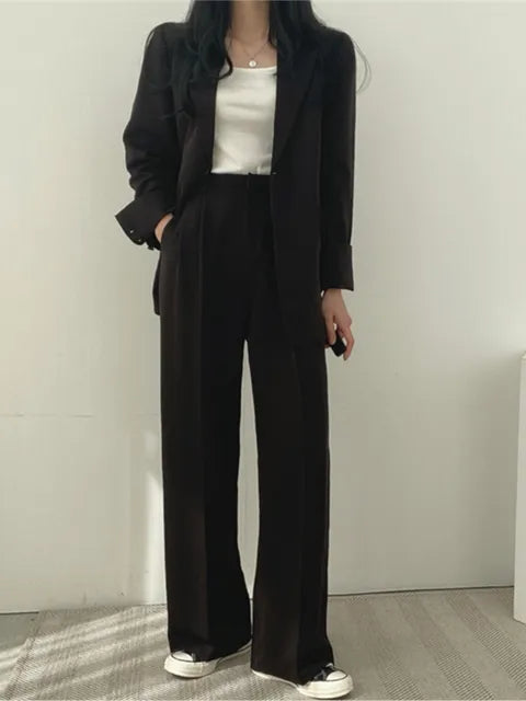 Frau in schwarzem Anzug mit weißem Top und Sneakers, modisch elegant, Business-Look, minimalistisch, moderne Damenmode, lässiger Stil.