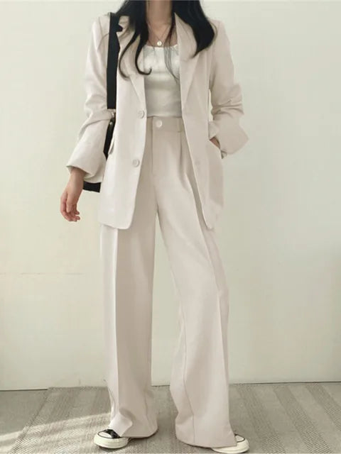 Frau in weißem Anzug mit weitem Blazer und Hose, trägt weiße Sneakers. Modetrend, Business-Casual, eleganter Look, minimalistisch, stilvoll.