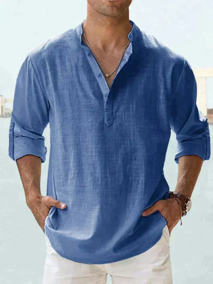 Mann in blauem Leinenhemd mit Stehkragen und Knopfleiste, lässig in weiße Hose gekleidet. Perfekt für Sommermode und Freizeitkleidung.