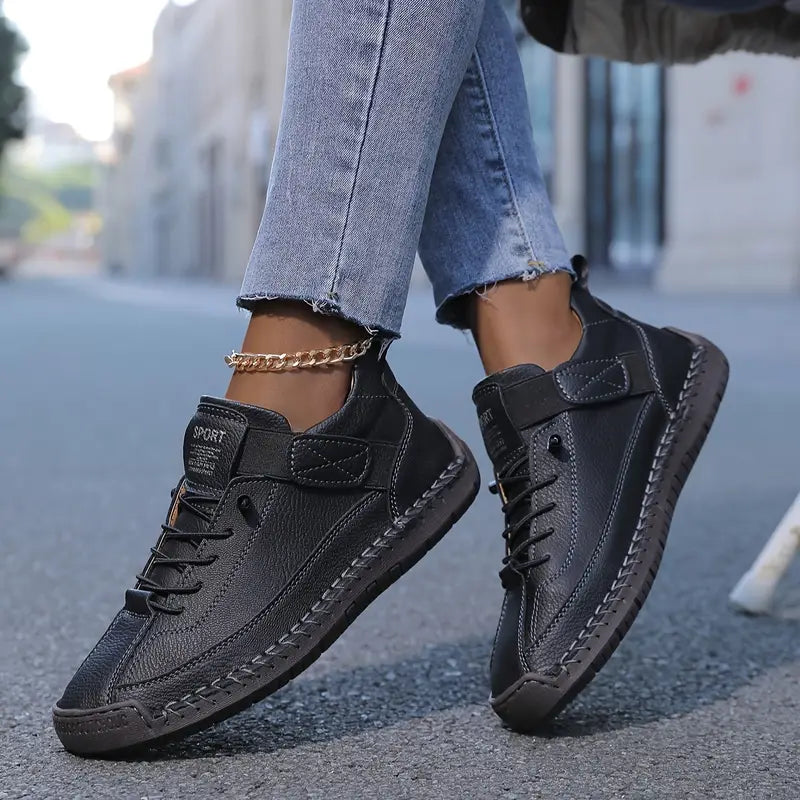 Schwarze Leder-Sneaker an den Füßen einer Person in blauen Jeans, die auf einer städtischen Straße geht. Modische, bequeme Freizeitschuhe für Damen.