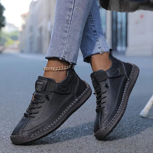 Schwarze Leder-Sneaker an den Füßen einer Person in blauen Jeans, die auf einer städtischen Straße geht. Modische, bequeme Freizeitschuhe für Damen.