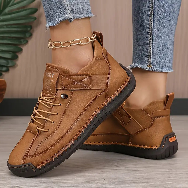 Braune Damen-Sneaker aus Leder mit Ziernähten, getragen mit Jeans und goldener Fußkette. Bequeme Freizeitschuhe, modisch und alltagstauglich.