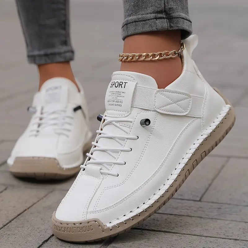 Weiße Sneaker mit brauner Sohle, getragen von Person mit grauer Jeans und goldener Fußkette. Modische Straßenschuhe, sportlicher Stil.