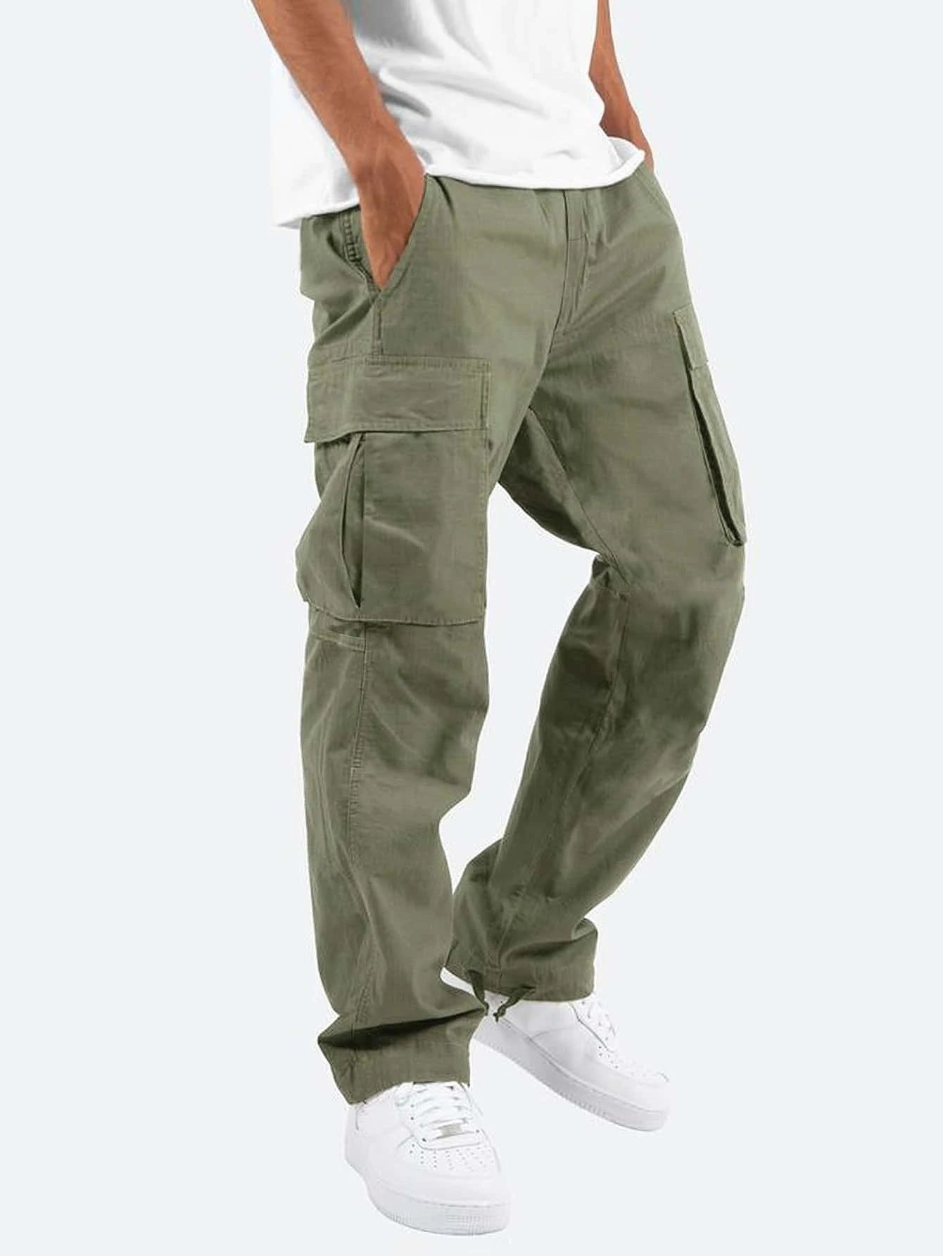 Mann trägt olivgrüne Cargohose mit Seitentaschen, kombiniert mit weißem T-Shirt und weißen Sneakers. Modetrend, lässiger Stil, Herrenbekleidung.