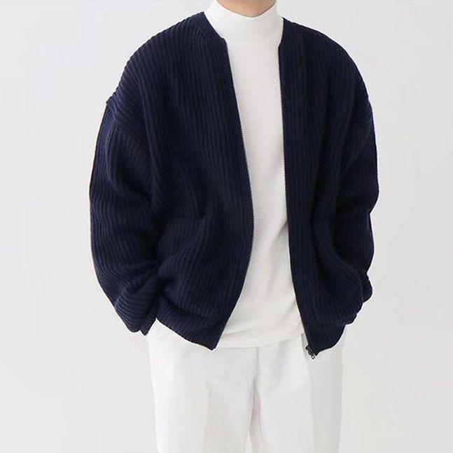 Person in weißem Rollkragenpullover und dunkelblauer, gerippter Strickjacke. Modischer, minimalistischer Look, ideal für Herbstmode.