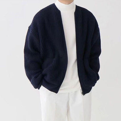 Person in weißem Rollkragenpullover und dunkelblauer, gerippter Strickjacke. Modischer, minimalistischer Look, ideal für Herbstmode.