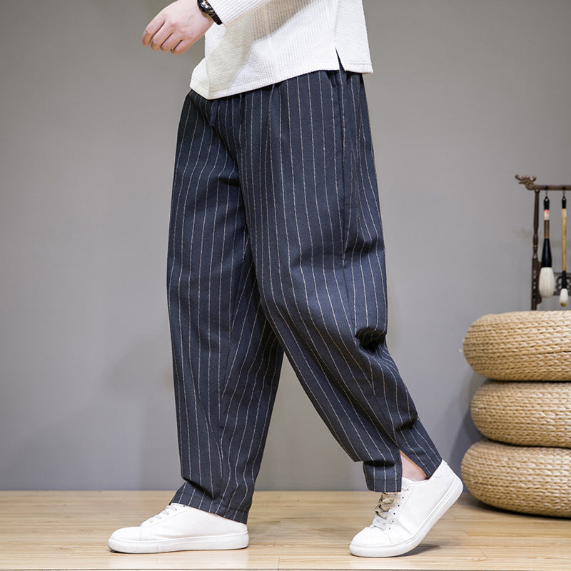 Person trägt weite, gestreifte Hose in Dunkelblau mit weißen Streifen und weiße Sneaker. Modetrend, Herrenbekleidung, lässiger Stil.