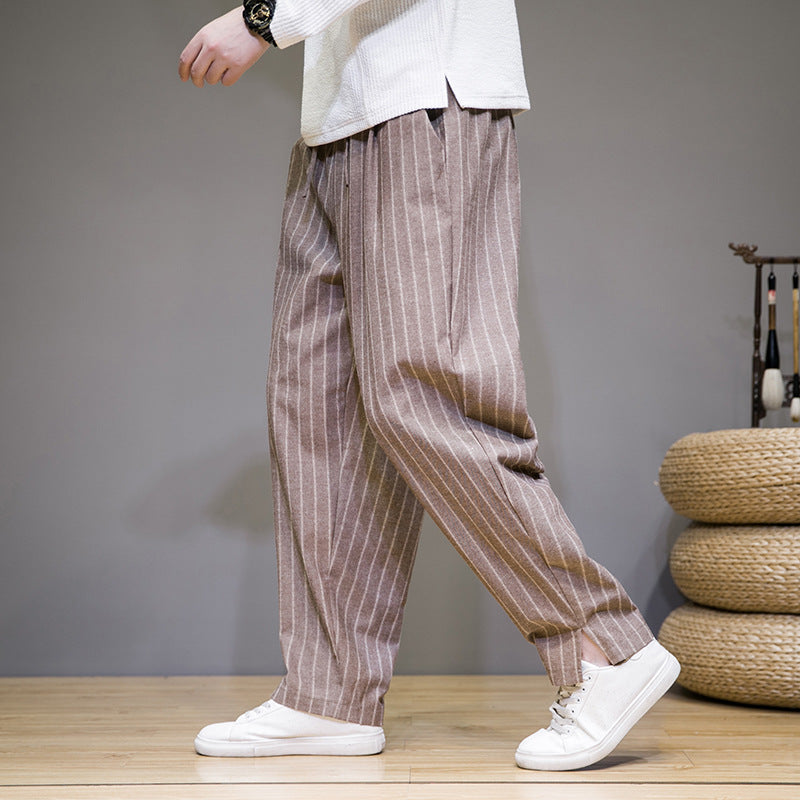 Mann in gestreifter, brauner Hose und weißen Sneakers auf Holzboden, seitliche Ansicht. Modetrend, Herrenbekleidung, lässiger Stil.