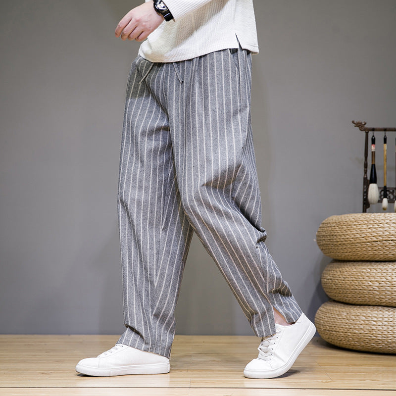 Graue gestreifte Herrenhose, lässig geschnitten, kombiniert mit weißen Sneakers. Moderne Herrenmode, ideal für Freizeit und Alltag.