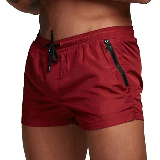 Rote Herren-Badeshorts mit elastischem Bund und schwarzen Kordeln, seitlichen Reißverschlusstaschen, ideal für Strand und Schwimmen.