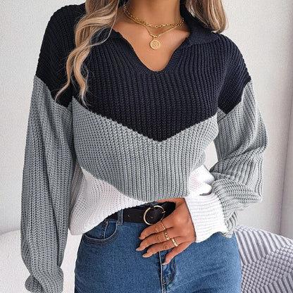 Frau trägt modischen Strickpullover in Schwarz, Grau und Weiß mit V-Ausschnitt, kombiniert mit blauer Jeans und goldener Halskette.