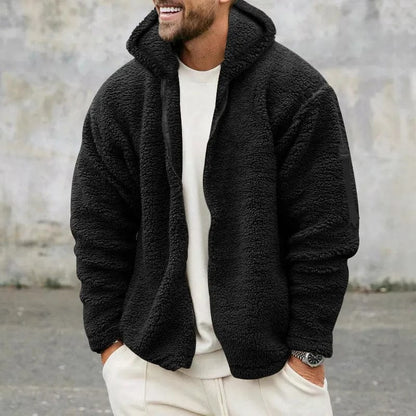 Mann in schwarzer Teddyfleece-Jacke und weißem Outfit, lächelnd, vor grauer Wand. Modetrend, Herrenbekleidung, Winterjacke, lässiger Stil.