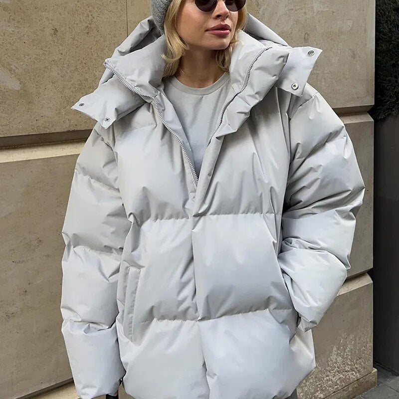 Frau in grauer Daunenjacke und Mütze vor Betonwand. Wintermode, warme Kleidung, stilvolle Damenjacke, Outdoor-Bekleidung.