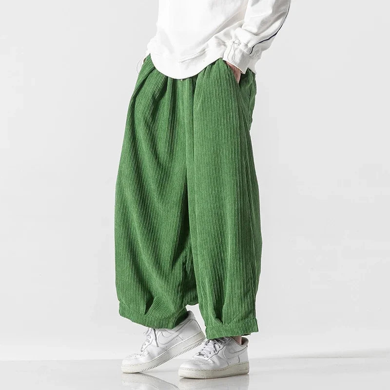 Grüne, weite Cordhose für Herren, kombiniert mit weißen Sneakers und einem weißen Oberteil. Modetrend, lässiger Stil, bequeme Herrenbekleidung.