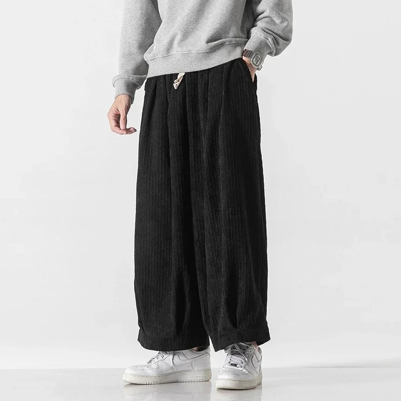 Graue Sweatshirt und schwarze, weite Cordhose, kombiniert mit weißen Sneakers. Modetrend, lässiger Streetwear-Look für Herren.