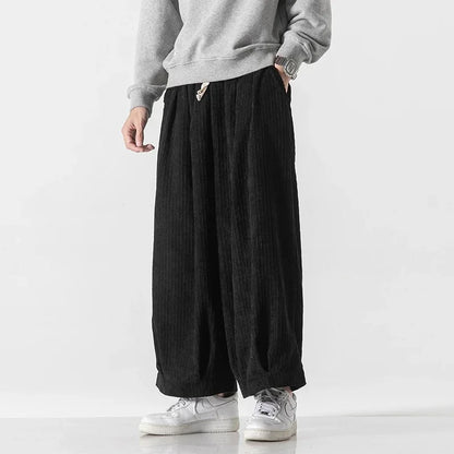 Graue Sweatshirt und schwarze, weite Cordhose, kombiniert mit weißen Sneakers. Modetrend, lässiger Streetwear-Look für Herren.