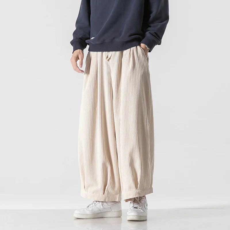 Person trägt weite, beige Haremshose und weiße Sneaker vor weißem Hintergrund. Modetrend, lässiger Stil, Herrenbekleidung, Streetwear.