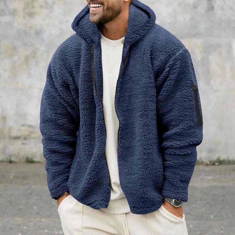 Mann in blauer Fleecejacke mit Kapuze, lässig gekleidet, steht vor grauer Wand. Wintermode, Herrenbekleidung, Outdoor-Jacke, gemütlich.