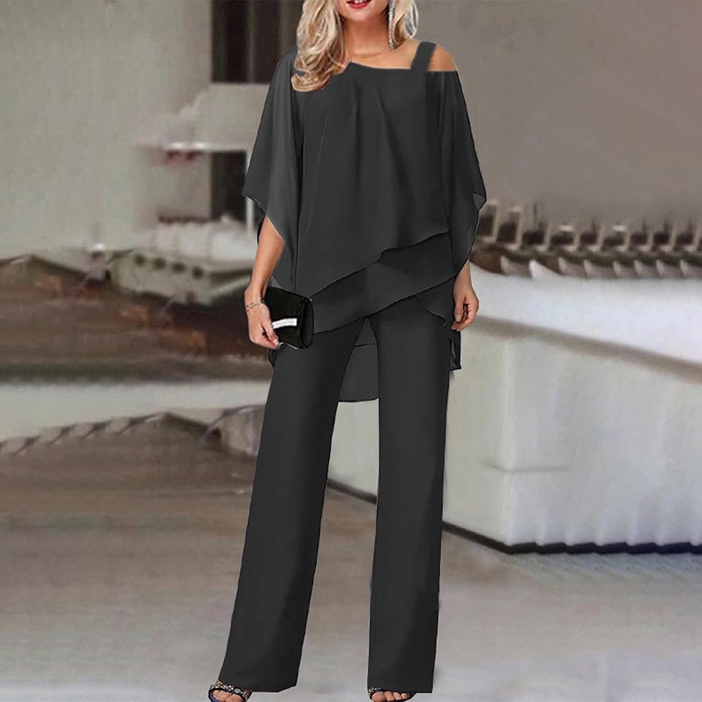 Elegante Frau in schwarzem, schulterfreiem Hosenanzug mit Clutch, stehend in modernem Innenraum. Modetrend, Damenbekleidung, Abendmode.