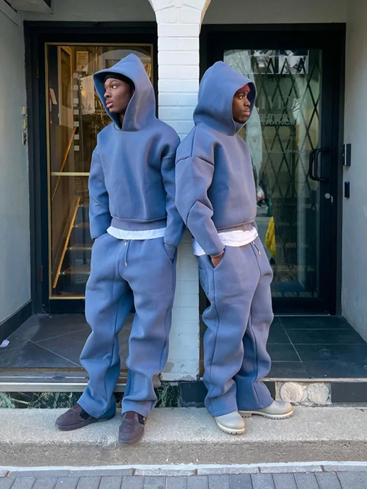 Zwei Personen in blauen Oversize-Hoodies und Jogginghosen stehen Rücken an Rücken vor einem Gebäude. Streetwear, Mode, urbaner Stil.