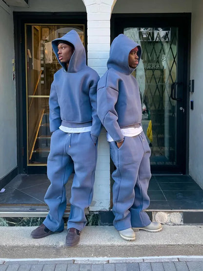 Zwei Personen in blauen Oversize-Hoodies und Jogginghosen stehen Rücken an Rücken vor einem Gebäude. Streetwear, lässiger Stil, urbane Mode.