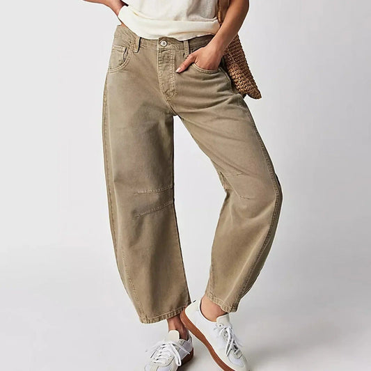 Damen in beigen Baggy-Jeans und weißen Sneakers, lässiger Look, Hand in der Tasche, modische Freizeitkleidung, neutraler Hintergrund.