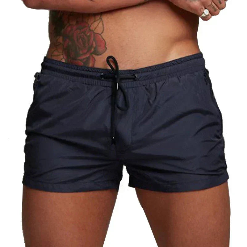 Mann mit dunkler Badehose und Rosen-Tattoo auf der Hüfte. Sommermode, Herren-Bademode, stilvolle Badebekleidung.