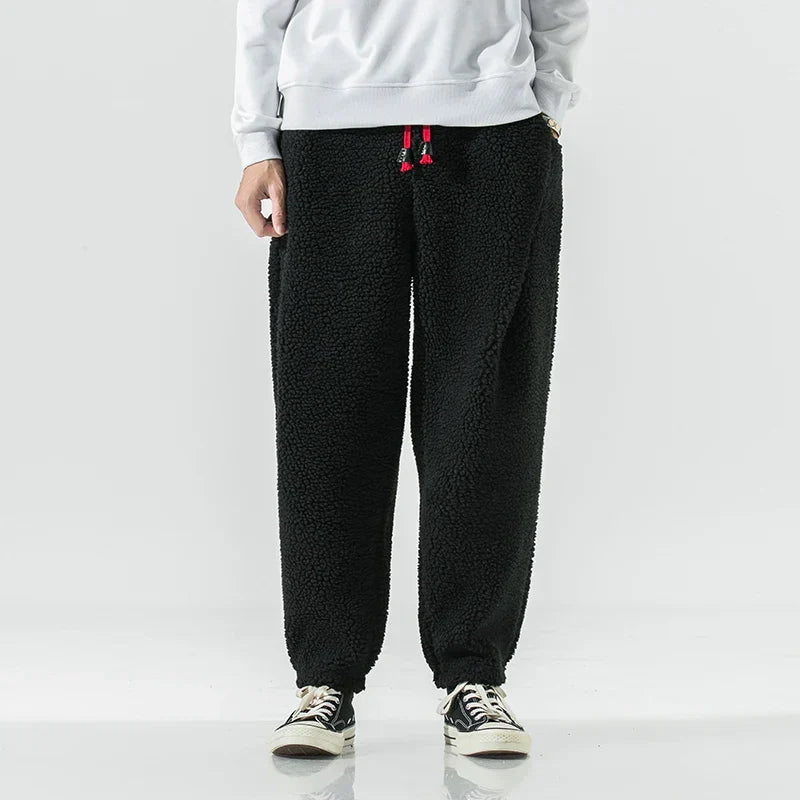 Schwarze Fleece-Jogginghose für Herren, lässiger Stil, kombiniert mit weißen Sneakers und grauem Sweatshirt. Bequem und modisch für den Alltag.