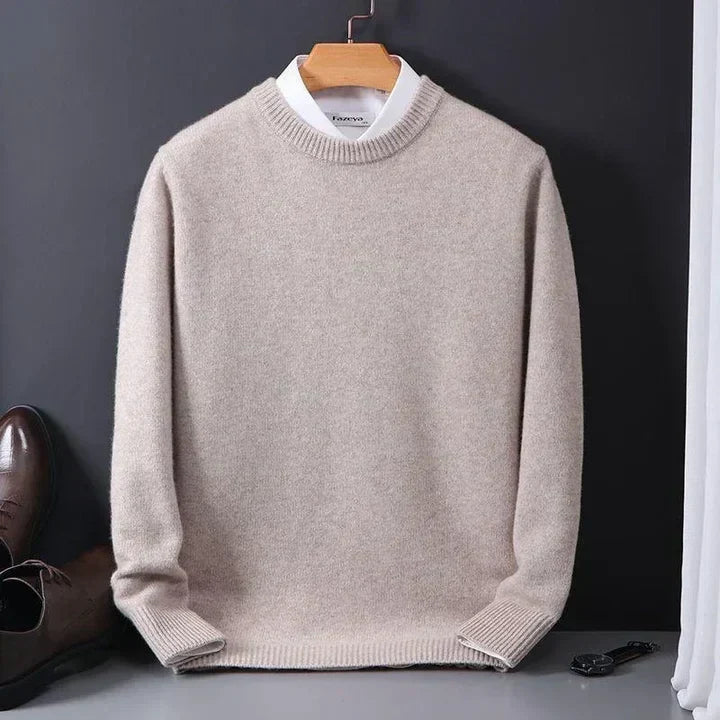 Beiger Herrenpullover aus Kaschmir, auf einem Kleiderbügel vor dunklem Hintergrund präsentiert, kombiniert mit weißem Hemd und braunen Lederschuhen.