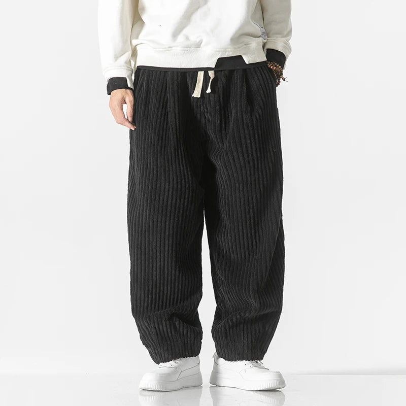 Mann in schwarzer, gerippter Cordhose und weißem Pullover, trägt weiße Sneaker. Modetrend, lässiger Stil, Herrenbekleidung, Streetwear.