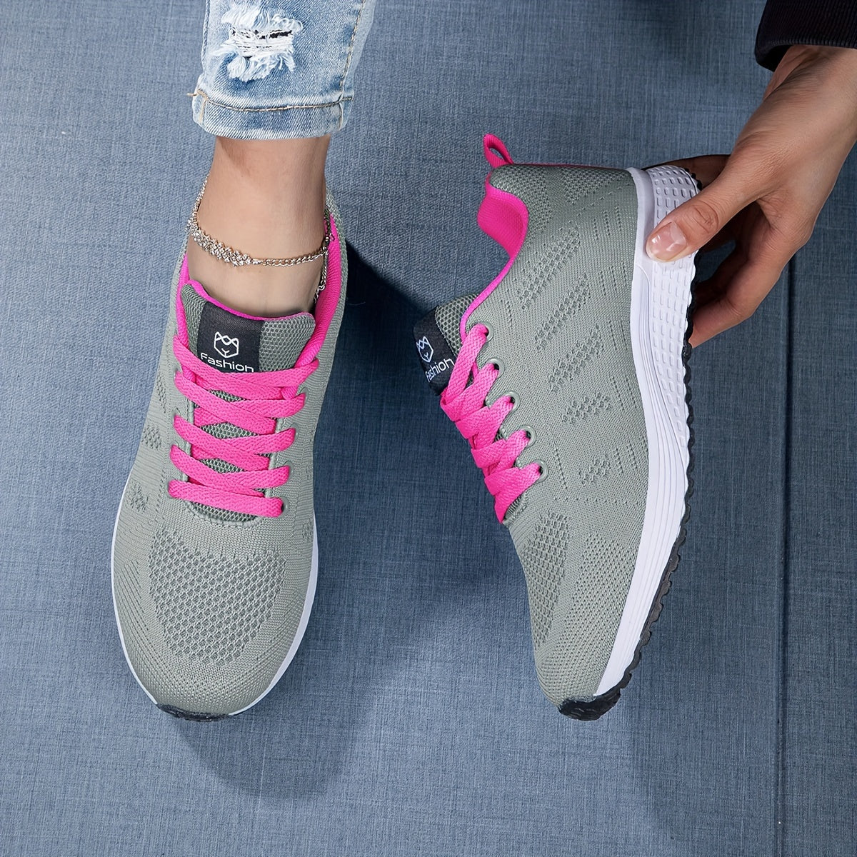 Graue Damen-Sneaker mit pinken Schnürsenkeln und weißer Sohle auf blauem Hintergrund. Modische Sportschuhe, ideal für Freizeit und Sport.
