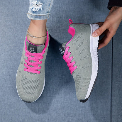 Graue Damen-Sneaker mit pinken Schnürsenkeln und weißer Sohle auf blauem Hintergrund. Modische Sportschuhe, ideal für Freizeit und Sport.