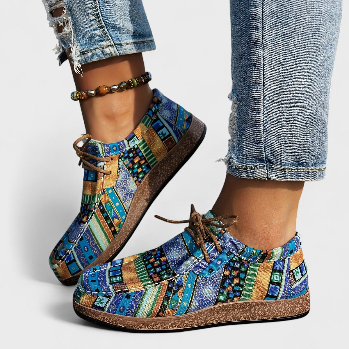 Bunte Patchwork-Sneaker mit blau-grünem Muster, getragen mit zerrissenen Jeans und Perlenfußkettchen. Modische Freizeitschuhe für Damen.