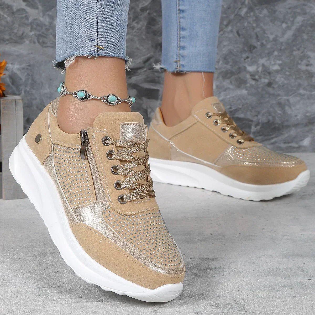 Beige Damen-Sneaker mit Glitzerakzenten, Reißverschluss und weißer Sohle, getragen mit blauer Jeans. Modische Schuhe für Freizeit und Alltag.