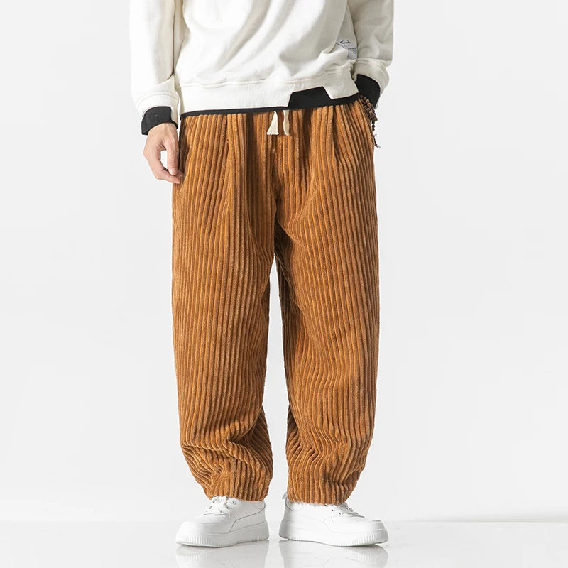 Mann in brauner Cordhose und weißen Sneakers vor weißem Hintergrund. Modetrend, Herrenbekleidung, lässiger Stil, Herbstmode.