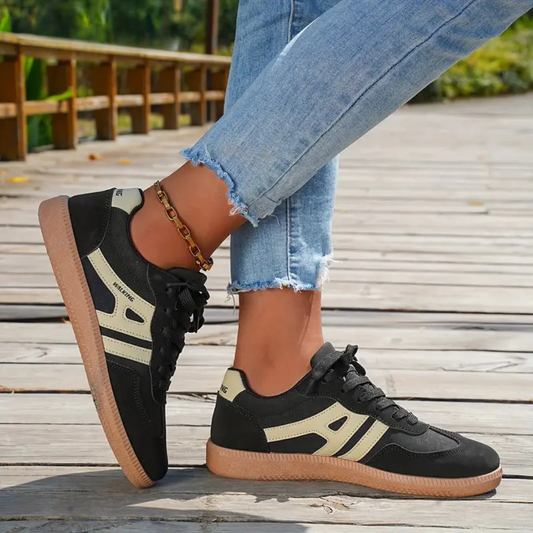 Schwarze Sneaker mit weißen Streifen, getragen von Person in blauen Jeans auf Holzsteg. Modische Damen-Sportschuhe, Freizeitlook, Outdoor.
