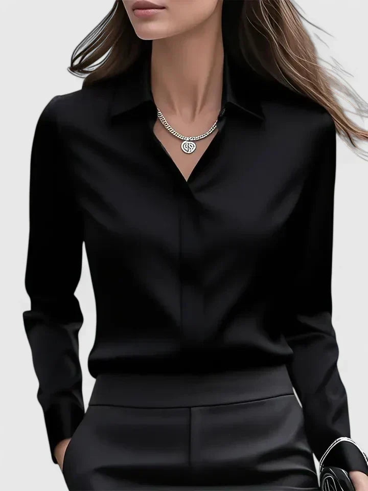 Frau in eleganter schwarzer Bluse und Hose, trägt eine silberne Halskette. Businessmode, stilvoll, modern, Damenbekleidung, Bürooutfit.