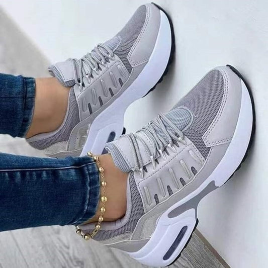 Graue Damen-Sneaker mit weißer Sohle, Mesh-Obermaterial und Schnürsenkeln, getragen mit blauer Jeans und goldfarbenem Fußkettchen.