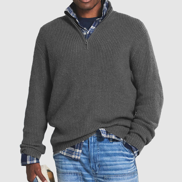 Grauer Herrenpullover mit Reißverschluss, kombiniert mit kariertem Hemd und blauer Jeans. Modischer Freizeitlook für Herbst und Winter.