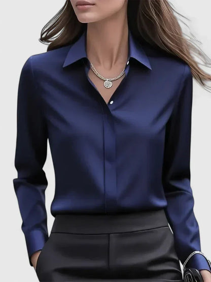 Frau in eleganter, dunkelblauer Seidenbluse mit Kragen und silberner Halskette, trägt schwarze Hose. Businessmode, Damenbekleidung, stilvoll.