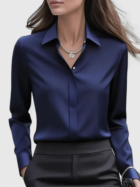 Frau in eleganter, dunkelblauer Seidenbluse mit Kragen und silberner Halskette, trägt schwarze Hose. Businessmode, Damenbekleidung, stilvoll.