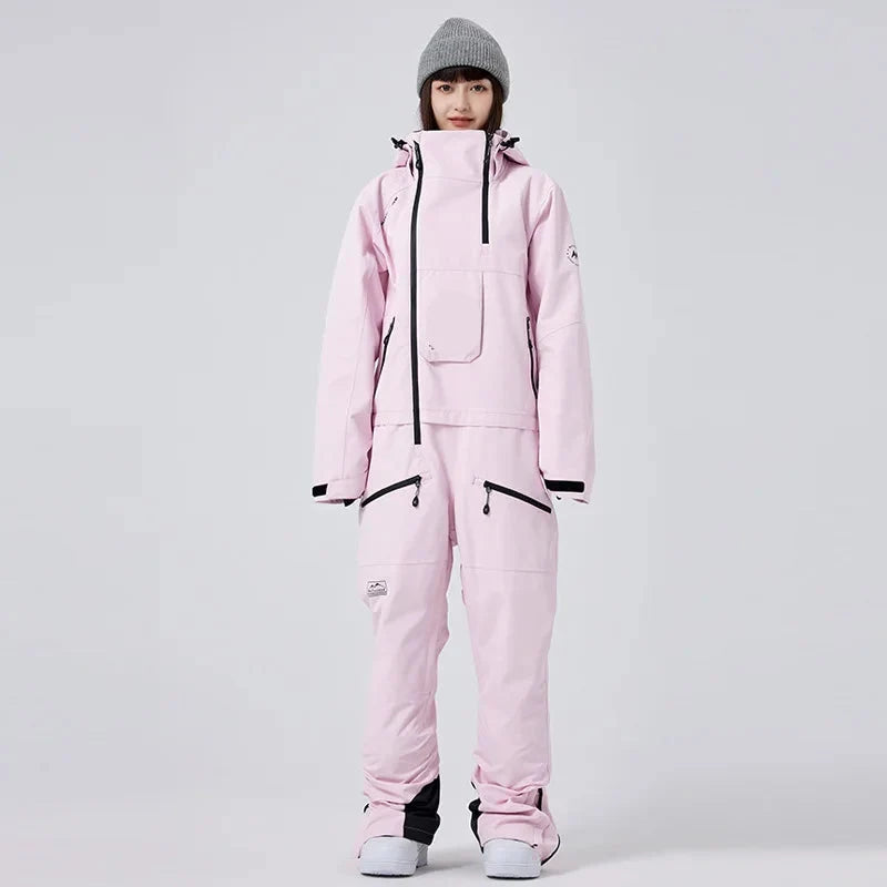 Frau in rosa Skianzug mit Kapuze und grauer Mütze, isoliert vor grauem Hintergrund. Wintermode, Skibekleidung, Outdoor-Ausrüstung.