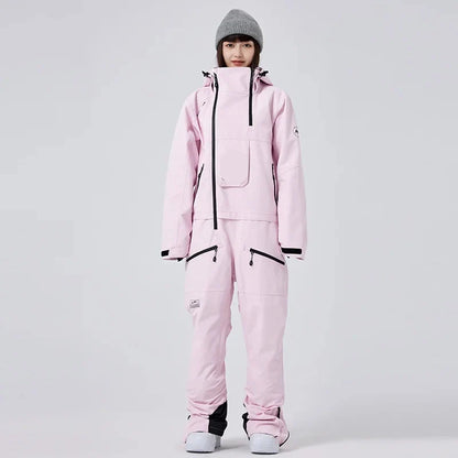 Frau in rosa Skianzug mit Kapuze und grauer Mütze, isoliert vor grauem Hintergrund. Wintermode, Skibekleidung, Outdoor-Ausrüstung.
