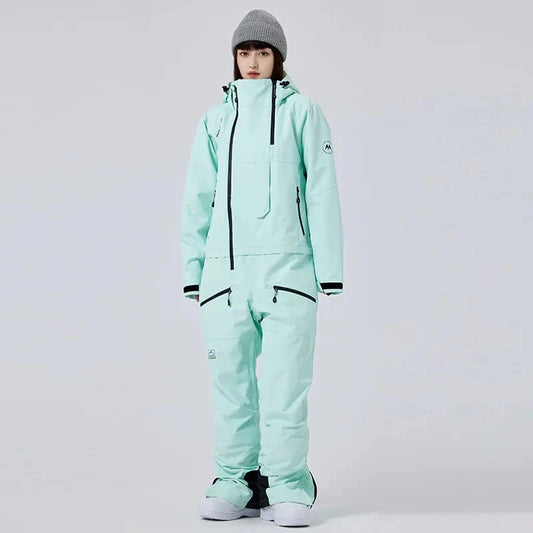 Frau in mintgrünem Skianzug mit Kapuze und grauer Mütze, isolierter Hintergrund. Wintermode, Skibekleidung, Outdoor-Ausrüstung.