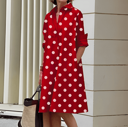 Frau in rotem, gepunktetem Kleid mit langen Ärmeln, hält eine Strohtasche. Stilvolle Mode, Sommerkleid, Polka-Dots, urbane Umgebung.