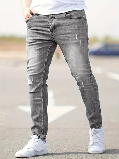 Graue Slim-Fit-Jeans für Herren, leicht zerrissen, kombiniert mit weißen Sneakers. Modischer Streetwear-Look, ideal für lässige Outfits.