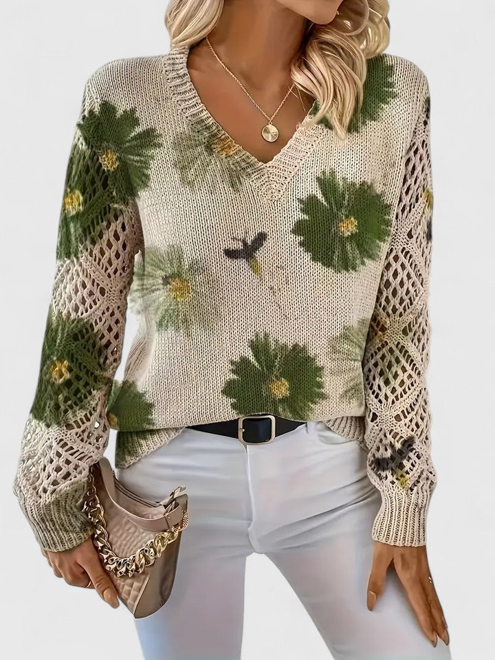 Damenpullover mit V-Ausschnitt, Blumenmuster und Strickdetails, kombiniert mit weißer Hose und beiger Handtasche. Modetrend Herbst 2023.